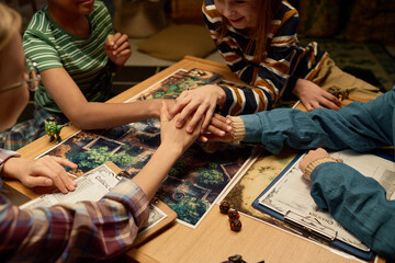 High angle of hand pile of four youthful intercultural friends on board with magic picture at the beginning or end of tabletop game