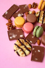 Pastel macarons, almond chocolate, peanut butter cookies and various nuts on bright pink background. Selective focus.