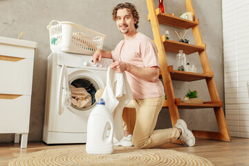 A handsome man in a pink shirt meticulously doing laundry at home.