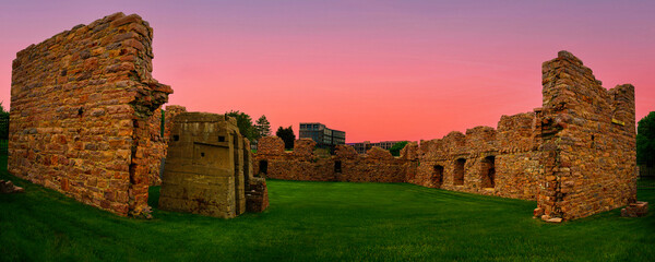 Queen Bee Mill Ruins Historical Place on the Big Sioux River Hilltop in Sioux Falls, South Dakota: The landmark quartzite rock walls, vibrant green hill, and pink sky at sunrise