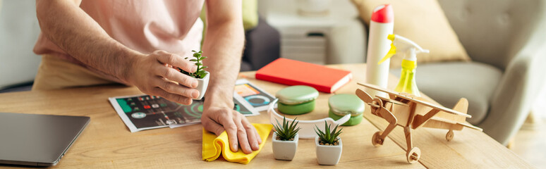 A handsome man in cozy homewear cleaning a table with a cloth.