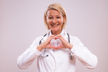 Portrait of mature female doctor  showing heart shape with hands on gray background.