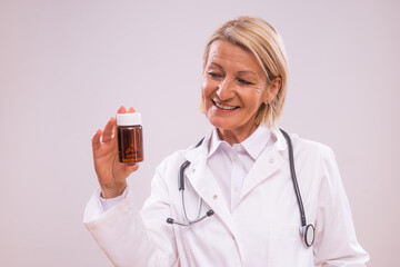 Portrait of mature female doctor  holding bottle of pills  on gray background.