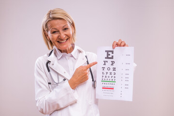 Portrait of mature female doctor  doing eye exam   on gray background.