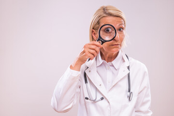 Portrait of shocked mature female doctor  with loupe on gray background.