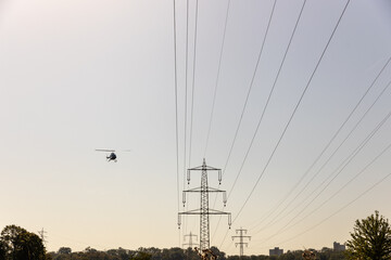 Helikopter fliegt nahe Hochspannungsleitungen über einem Feld bei sonnigem Himmel