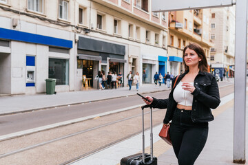 A traveler with her suitcase waiting for the arrival of the tram