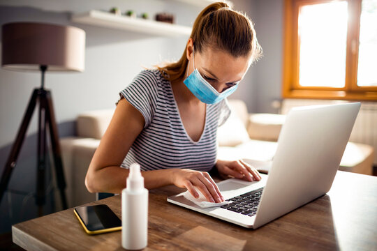 Woman disinfecting laptop keyboard with cleaning wipe