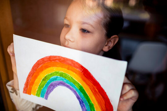 Little girl holding up rainbow drawing she made
