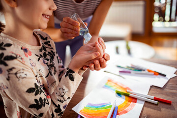 Mother giving daughter hand sanitizer while doing crafts at home