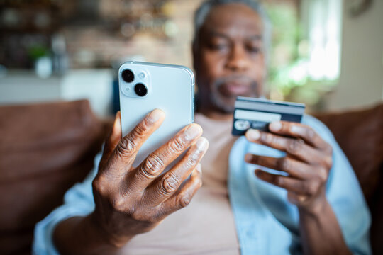 Senior man using smartphone and credit card for online shopping at home