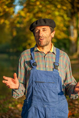 Portrait of a Frenchman, wearing a beret and blue dungarees smiling and gesticulating to camera