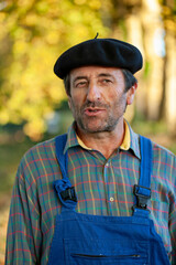 Portrait of a Frenchman, wearing a beret and blue dungarees smiling and gesticulating to camera