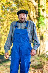 Portrait of a Frenchman, wearing a beret and blue dungarees smiling and gesticulating to camera