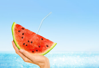 watermelon slice with a glass tube in a woman’s hand against the background of the sea, summer...