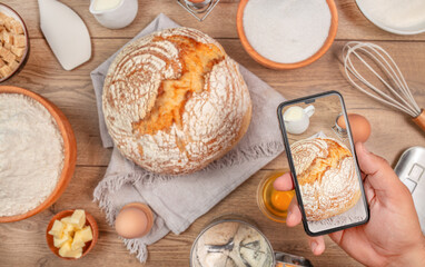 Man holding a smart phone hands close up, kitchen table worktop on background with bread and utensils. Food recipes, online delivery, homemade food, cooking process