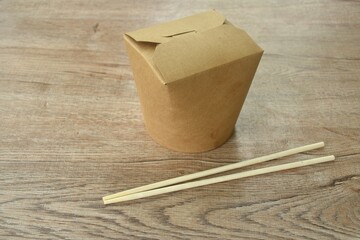 noodles packaged in hard brown paper box for take home with wooden chopsticks on table