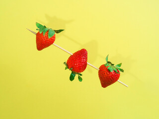 Creative layout with copy space made of strawberries on wooden stick against pastel yellow background. Copy space. Creative summer idea. Minimal fruit concept.