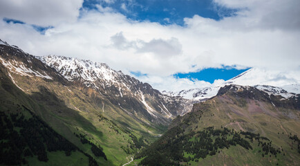 Fototapeta premium Green wooded mountains and around high mountains in the snow and a beautiful sky on a summer day. Georgia.