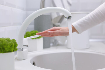A girl opens the water in the tap in the kitchen in a modern interior. Purified water, hygiene