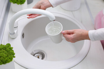 A girl pours clean water into a glass from a kitchen tap. Purified water