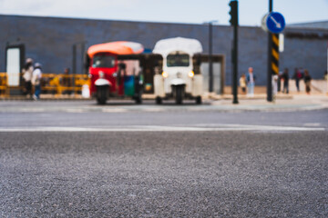 Obraz premium Asphalt road in the city of Lisbon and in the background, out of focus, 2 tuk tuk cars.