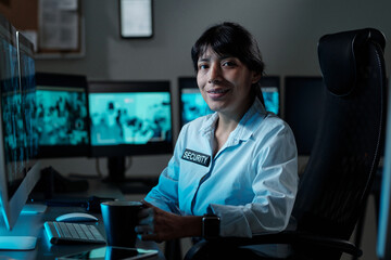 Young successful female security guard looking at camera with smile while sitting by workplace with...