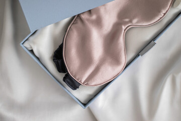 Beige sleeping mask lies in gift box on white bed. Silk sleep mask with boxes.