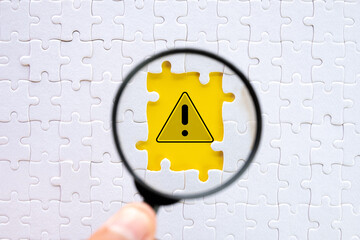 Magnifying Glass Focusing on Exclamation Mark in Breakthrough Yellow Paper Hole Among Puzzle Pieces Sign Highlighting Safety and Hazard Prevention,caution sign, alertness in risky situations.