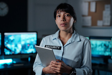 Young serious Hispanic female officer of surveillance room with tablet in hand looking at camera...