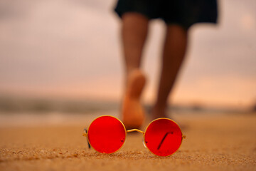 feet on the beach, cropped shot view of men legs on the sandy beach, Fashionable colourful sunglasses, A tourist walks along the beach