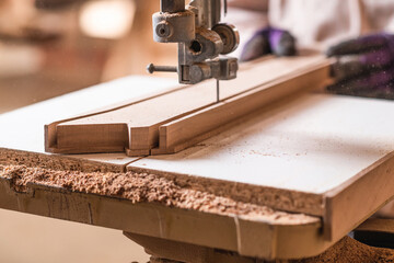 Carpenter’s hands using band saw machine tool, cutting piece o