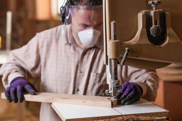 Skilled carpenter using band saw machine, wearing safety gloves