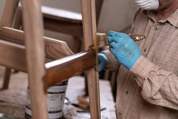 Carpenter varnishing chair with brush in a workshop