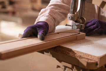 Worker in the carpentry workshop cuts the wooden board using ban