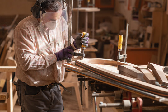 Carpenter uses tight wood clamps for wooden plank - wearing safety equipment in carpentry workshop.