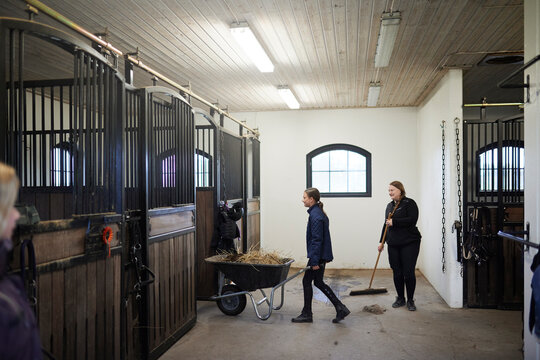 Girl and female farmer cleaning stable together
