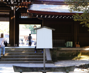 Old, empty wooden grey, dark brown sign stands next to entrance to temple in Japan. People walking...