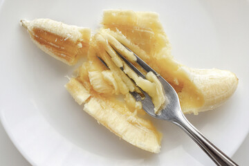 Ripe banana being mashed with a fork on a white plate. Banana puree on a plate.  Healthy and...