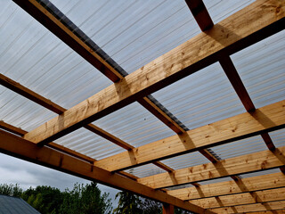 terrace with wooden pergola and plexiglass roof. vines are straining, crawling under the beams....