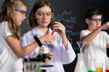 Teacher in support and watch student in laboratory they wear safety glasses, stand and experiment about science of chemistry in STEM class. Student funny do experiment with liquid in tube. Erudition.
