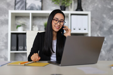 Fototapeta premium A successful Korean businesswoman multitasking with a laptop and phone, managing her business with confidence.