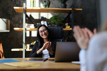 In the office, an Asian businesswoman celebrates victory, clapping happily with her team, sharing...