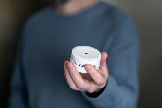 Midsection of man holding smoke detector at home