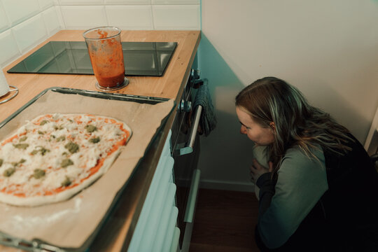 High angle view of young woman crouching while looking at oven under kitchen counter at home