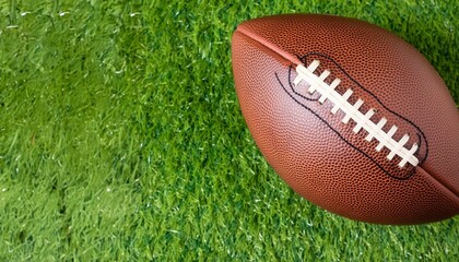 Brown American football ball on green artificial stadium turf background. Top view
