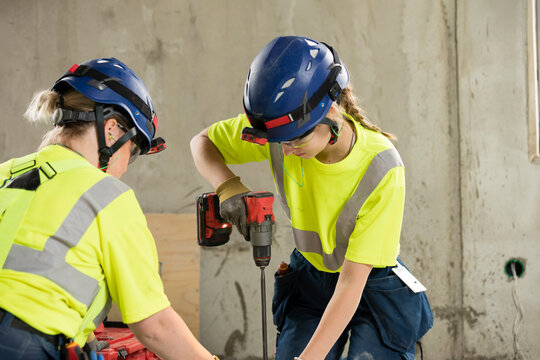 Female engineer using drill while working with coworker at construction site