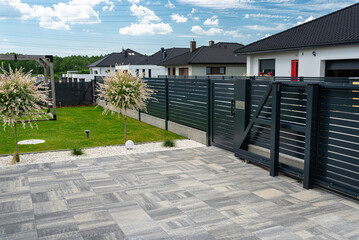 A modern panel fence in anthracite color, a visible sliding gate to the garage and a wicket with a...