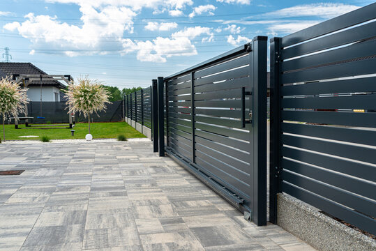 A modern panel fence in anthracite color, visible sliding gate to the garage and a slab driveway.