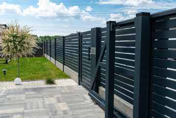 A modern panel fence in anthracite color, a visible sliding gate to the garage and a wicket with a letterbox.